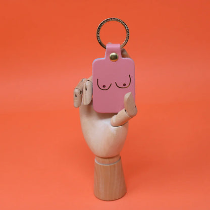 Różowy skórzany brelok Boobs pale pink marki Ark Colour Design trzymany w dłoni na pomarańczowym tle.