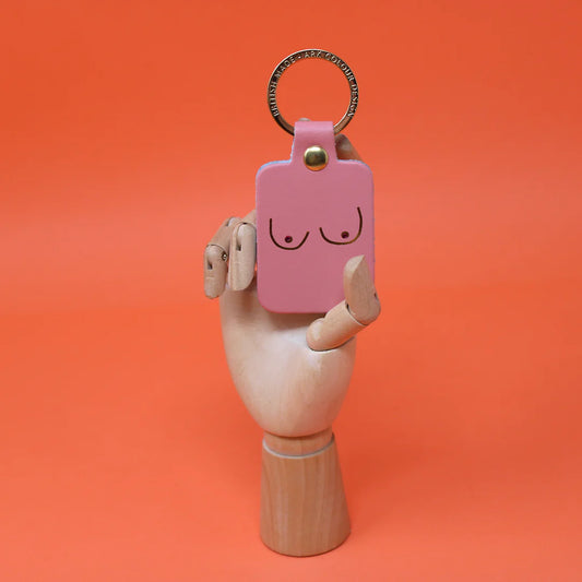 Różowy skórzany brelok Boobs pale pink marki Ark Colour Design trzymany w dłoni na pomarańczowym tle.