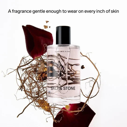 Flakon mgiełki Salt & Stone Black Rose & Oud w otoczeniu płatków róży i korzeni.